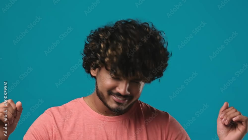 Young indian bearded guy with curly hair wearing t-shirt dancing over blue studio background Young indian bearded guy with curly hair wearing t-shirt dancing over blue studio background