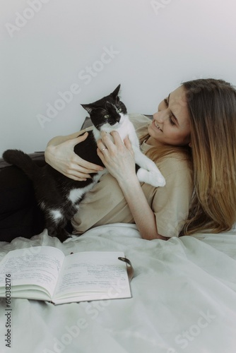 Cats friendly. Attractive young woman playing with her cat and smiling while lying in bed at home. Photo with place for text