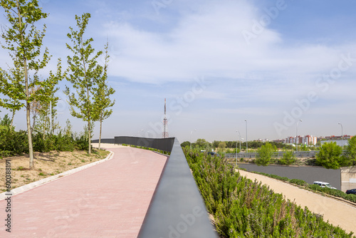 A walkway with red brick pavement and metal railing in a new urban park