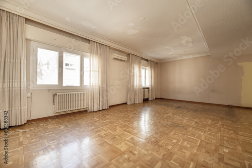 A large empty room in a house with parquet floors  several windows with curtains