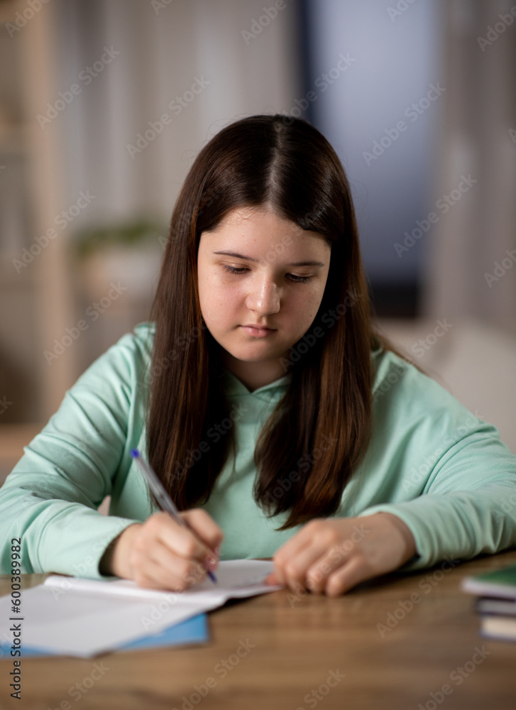 Focused schoolgirl doing homework at her desk. Little girl writing in her notebook, home schooling Focused schoolgirl doing homework at her desk. Little girl writing in her notebook, home schooling