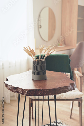 live edge wooden slab coffee table with cement vase and wheat stems. vertical shot of cozy place in home.