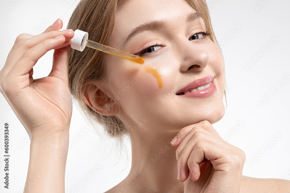 Close-up portrait of a beautiful girl applying an oil serum moisturizer to her face