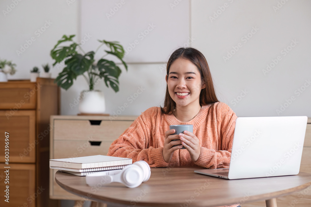 Beautiful young smiling woman working enjoying on laptop and drinking coffee while sitting comfortable at home Beautiful young smiling woman working enjoying on laptop and drinking coffee while sitting comfortable at home