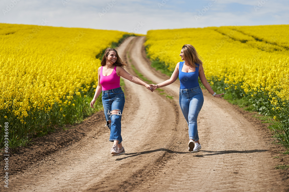 Plus size women walking on a road through canola fields together holding hands Plus size women walking on a road through canola fields together holding hands