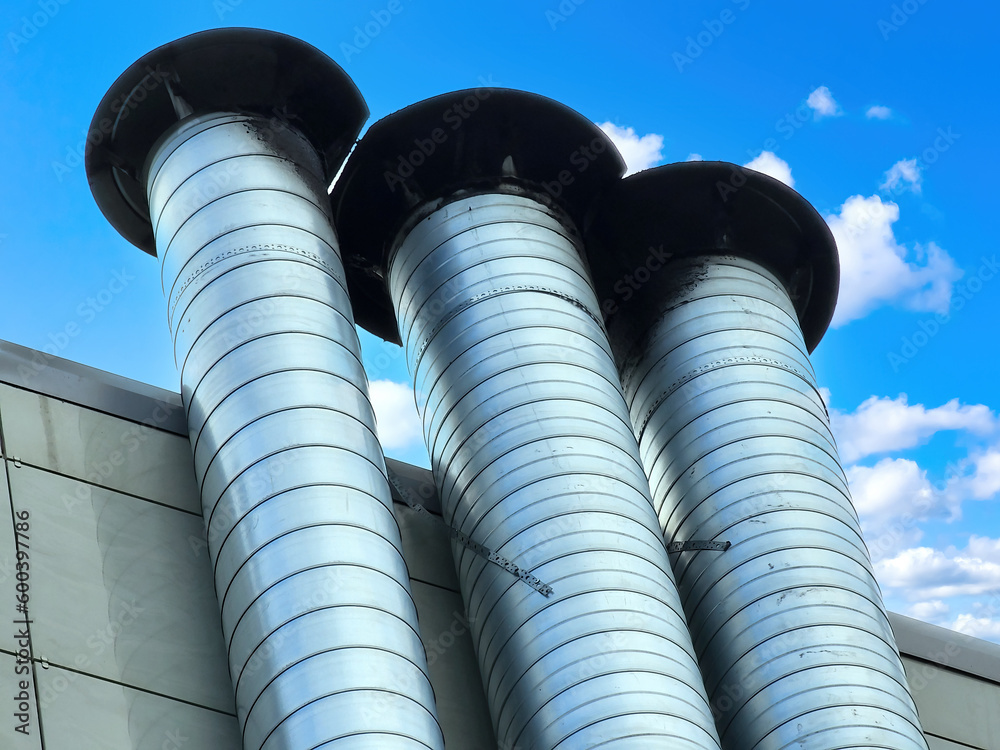 Metal chimney pipes. Boiler room wall with pipes for steam outlet. Chimney system. Fragment of facade under blue sky. Steel pipes on building. Chimney of restaurant or manufacturing company Metal chimney pipes. Boiler room wall with pipes for steam outlet. Chimney system. Fragment of facade under blue sky. Steel pipes on building. Chimney of restaurant or manufacturing company