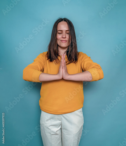 Woman with dark straight hair holds arms folded in front of chest. Meditation. Blue background.