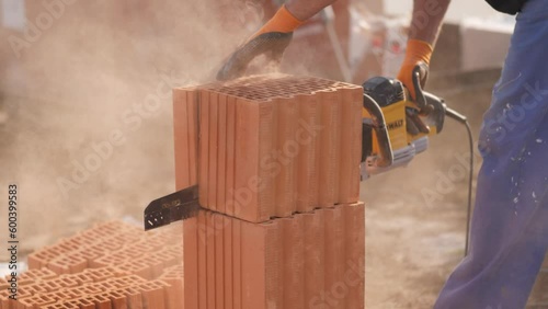sunny close-up shot of this construction worker cutting sawing through bricks for a bricklayer wall, dust floats in the air with sun shining on the dustclouds. dusty construction site. photo