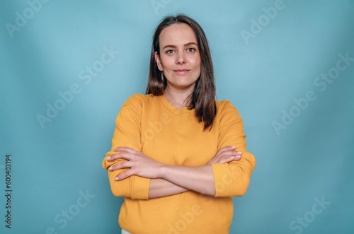 Smiling stylish woman with dark hair. Intertwined hands. Yellow sweater. Blue background.