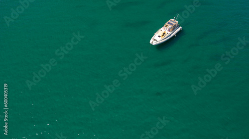 Aerial view of a white small boat anchored in the middle of the Mediterranean sea. 