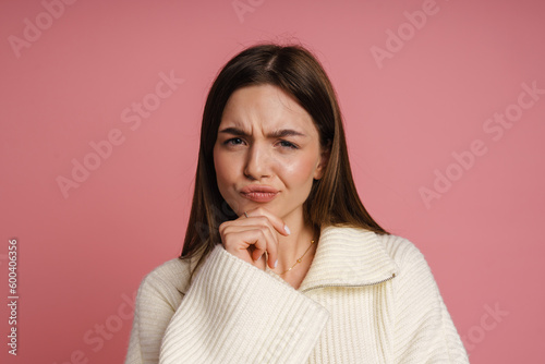 Canvas Print Pensive woman touching her chin and frowning while standing isolated over pink w