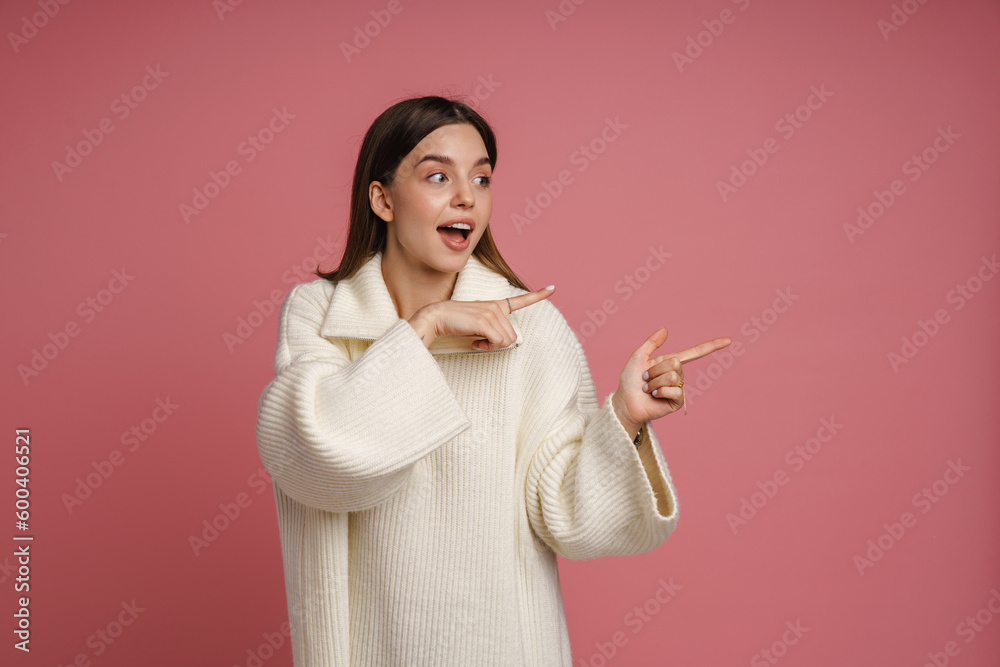 Excited woman pointing fingers away at copy space isolated over pink background Excited woman pointing fingers away at copy space isolated over pink background