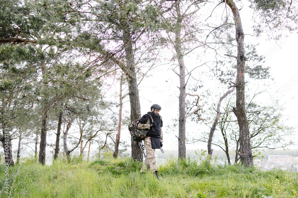 Young soldier in uniforms and tactical vest works in the forest and prepares for action at a temporary forest base. A man does in the work of demining the territory Young soldier in uniforms and tactical vest works in the forest and prepares for action at a temporary forest base. A man does in the work of demining the territory
