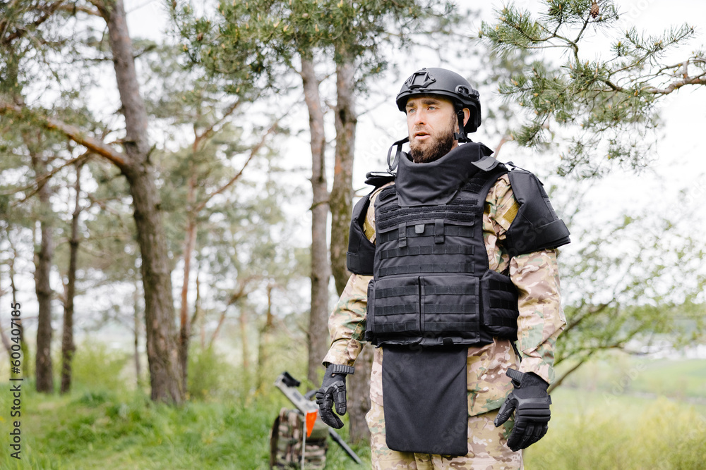 Young soldier in uniforms and tactical vest works in the forest and prepares for action at a temporary forest base. A man does in the work of demining the territory Young soldier in uniforms and tactical vest works in the forest and prepares for action at a temporary forest base. A man does in the work of demining the territory