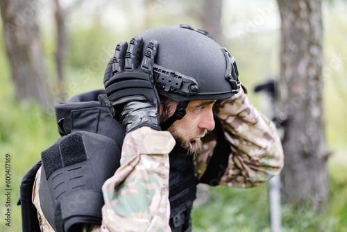 A man in a military uniform and a bulletproof vest works in the forest to demine the territory. A man puts on a protective helmet before starting work