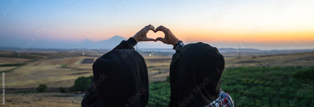 Young couple showing a heart at sunset