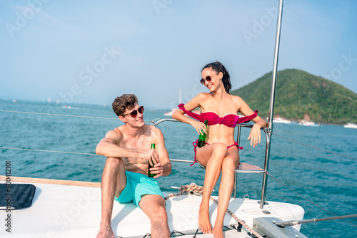 Portrait of happiness Caucasian couple drinking beer to party in yacht. Attractive man and woman hanging out celebrating anniversary in honeymoon trip while catamaran boat sailing during summer sunset