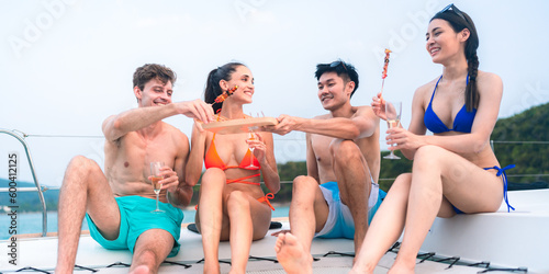 Fototapeta Naklejka Na Ścianę i Meble -  happy man in swimwear and woman in bikini having laugh fun in summer trip with friends group by eat bar-b-q grill and wine party drink, friendship vacation travel on sailboat yacht at the ocean sea