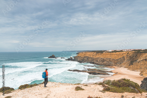 Backpacker enjoys his hike along the Fisherman Trail, Portugal. View of Alteirinhos Beach near Zambujeira do Mar, Odemira region. Atlantic Ocean, rocky cliffs and beach photo