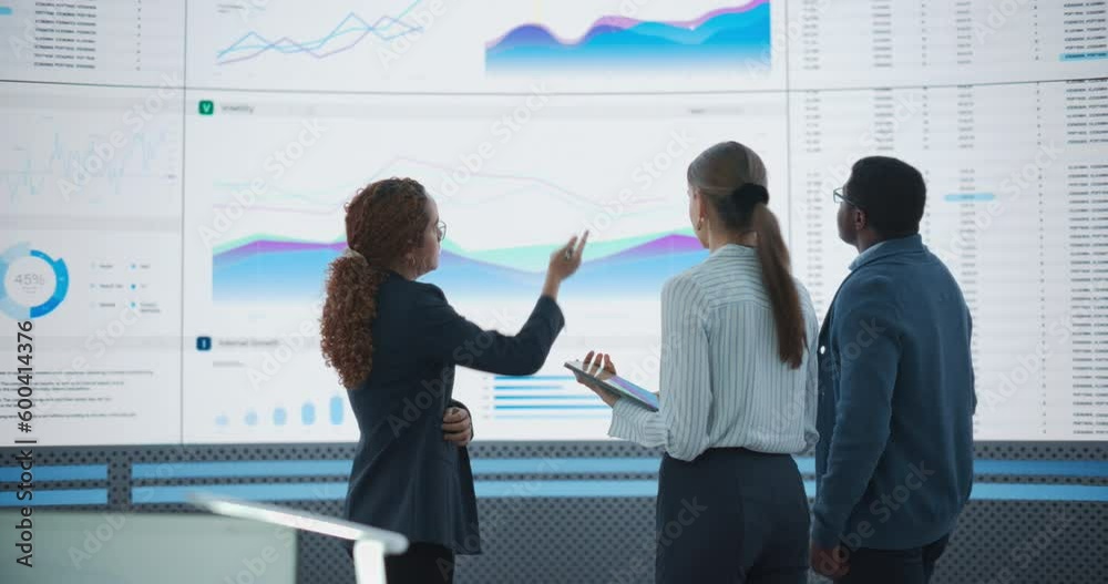 Diverse Team Of Data Scientists Analyzing Information And Graphs On Big Led Wall In Modern Monitoring Office. Multiethnic Colleagues Discussing Financial Strategies, Risk Factors, Potential Deals.