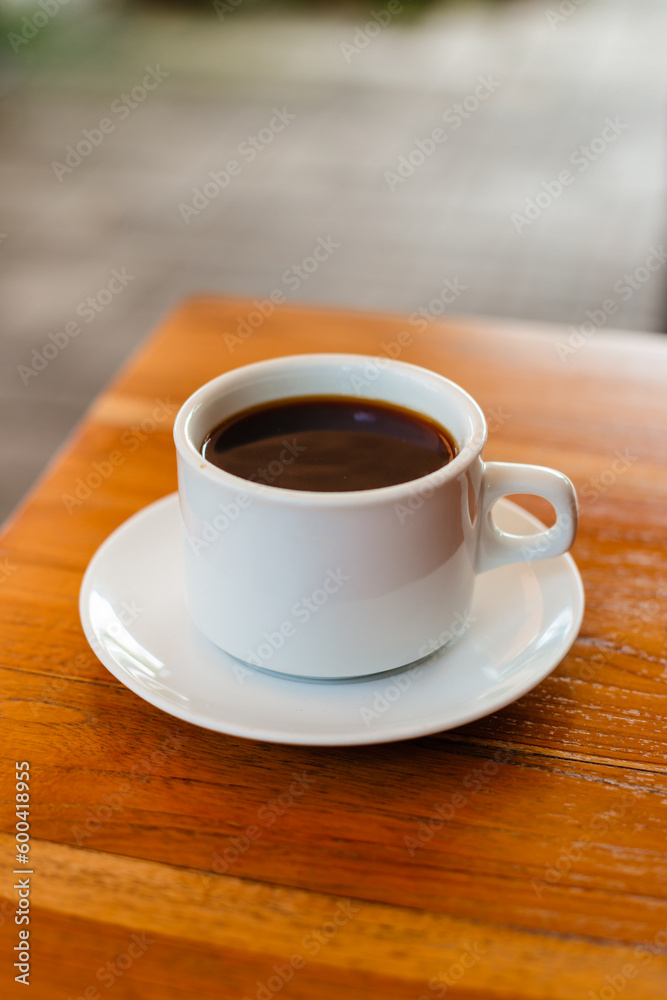 Black hot Americano in a white mug on a wooden table. Strong coffee made from natural beans for breakfast