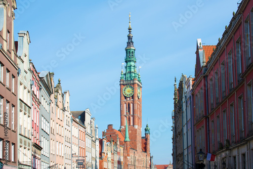 View of the old Catholic church with green tower and clock, and ancient buildings against the blue sky. Old architecture. Cityscape. Poland, Gdansk, April 2023
