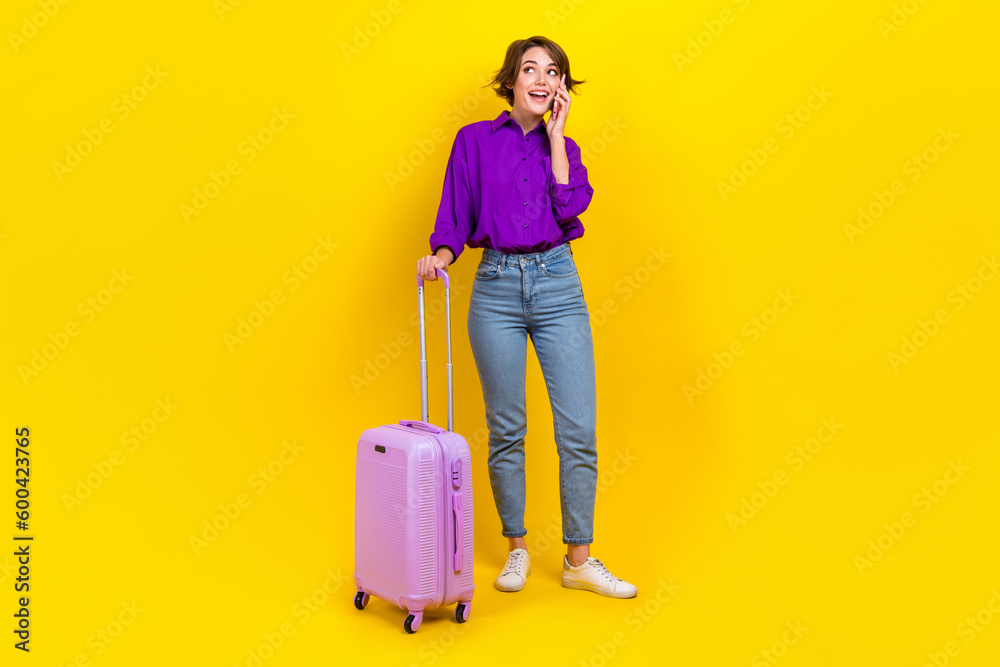 Full length photo of funky dreamy woman dressed purple shirt suitcase talking gadget looking empty space isolated yellow color background Full length photo of funky dreamy woman dressed purple shirt suitcase talking gadget looking empty space isolated yellow color background