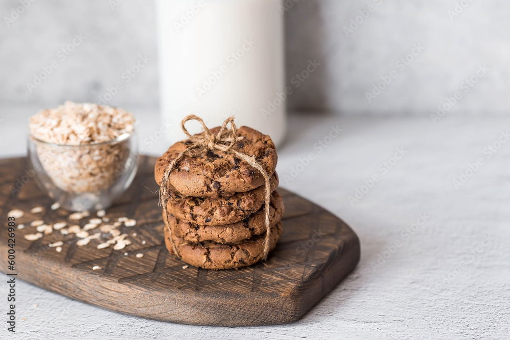 Organic natural cow's milk in a glass bottle, oatmeal and oatmeal cookies on a stylish wooden board on a stone table. Natural eco-friendly products. Organic natural cow's milk in a glass bottle, oatmeal and oatmeal cookies on a stylish wooden board on a stone table. Natural eco-friendly products.