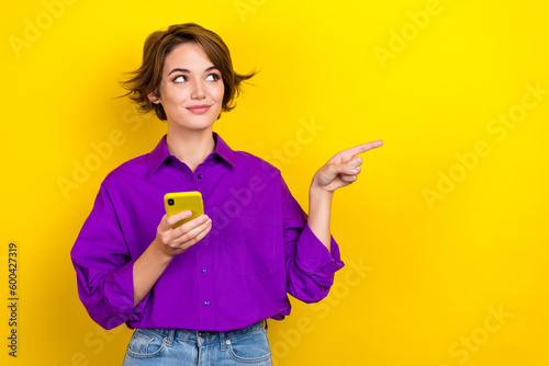 Photo of charming person hold smart phone look direct finger empty space wear violet isolated on yellow color background
