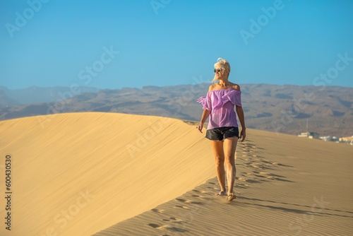 A tourist woman visiting the Maspalomas Dunes of Gran Canaria wearing comfortable clothing and shoes suitable for walking on sand.