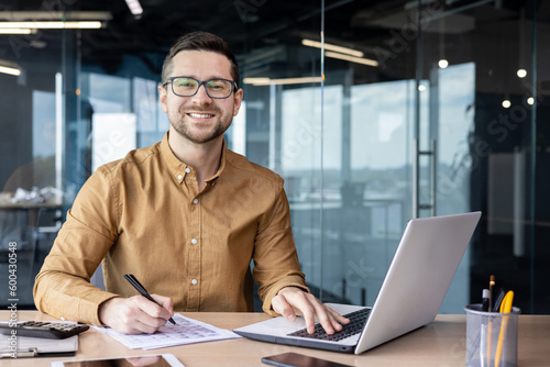Portrait of young businessman in shirt, man smiling and looking at camera at workplace inside office, accountant with calculator behind paper work signing contracts and financial reports