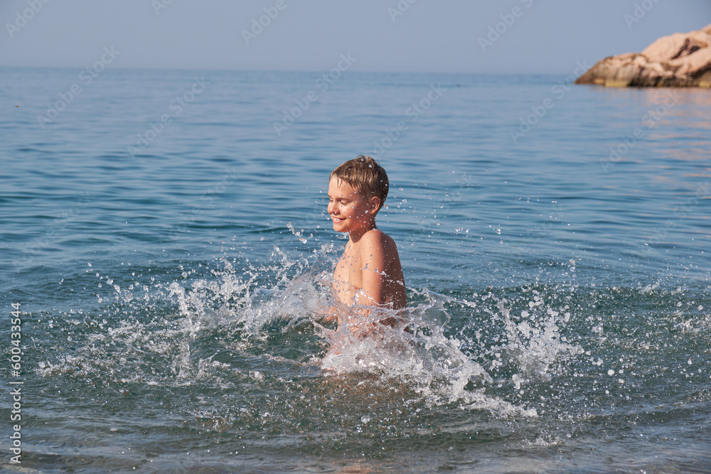 Happy joyful teen boy swim and splash in sea. Sunny summer day, holiday vacation