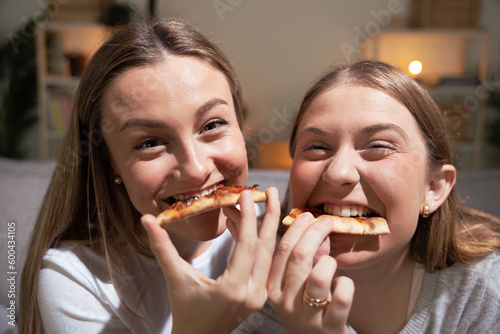Two blonde women eating pizza and looking at camera.