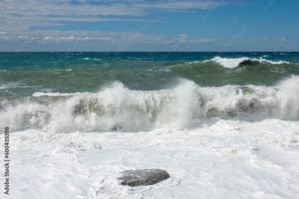 Large waves breaking over a rocky beach. Mediterranean storm on a sunny day