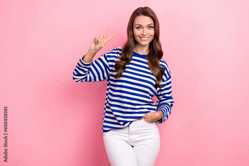 Photo of pleasant nice looking woman with wavy hairdo dressed striped shirt show v-sign arm in pocket isolated on pink color background Photo of pleasant nice looking woman with wavy hairdo dressed striped shirt show v-sign arm in pocket isolated on pink color background