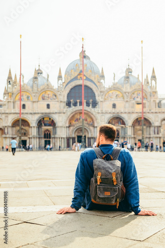 young man sitting on the ground looking at cathedral saint marco church