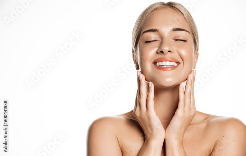 Portrait of happy smiling blond woman touches her face with pleasure, enjoys skincare cosmetic after effect, washes her skin with cleansing gel, hyaluronic acid for smooth face without blemishes photo
