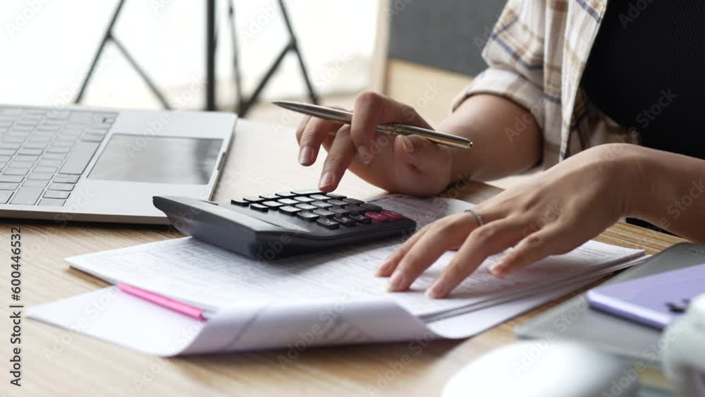 Close up hand of woman using calculator for calculate checking bills, taxes, bank account balance and calculating expenses in the living room at home.