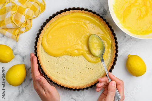 The process of cooking lemon tart. Filling the shortbread
tartlet  with lemon curd. Hands in the frame.Top view
