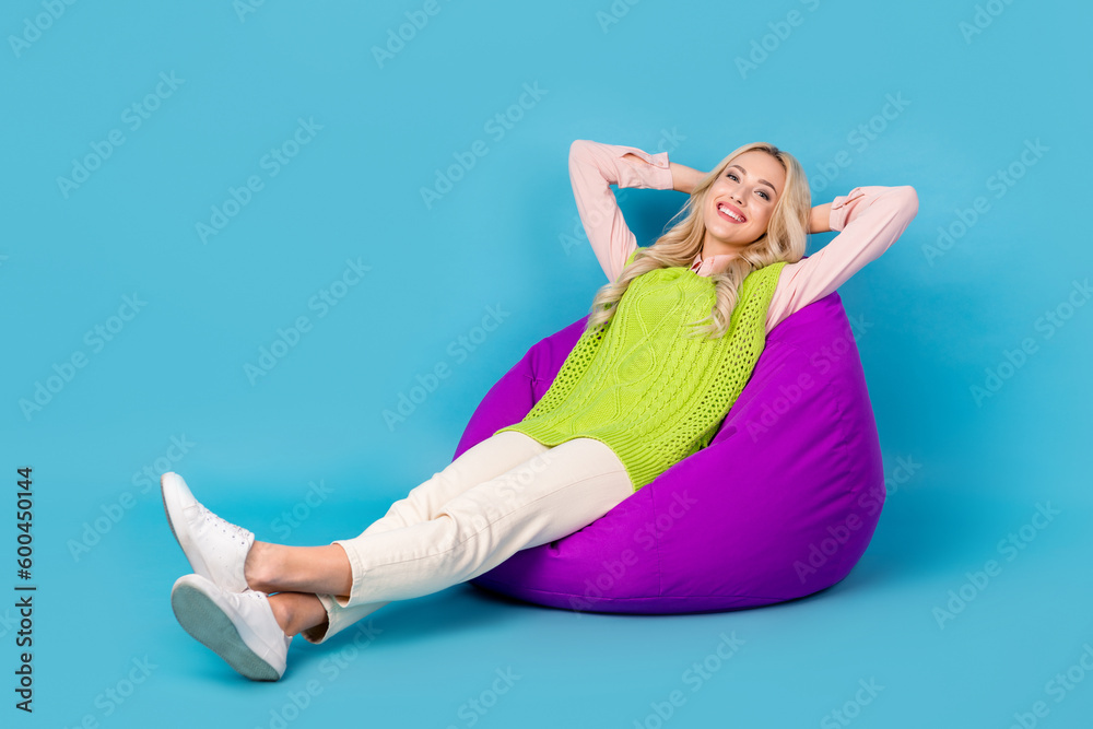Obraz premium Full size photo of cheerful nice girl sit cozy bag arms behind head enjoy free time isolated on blue color background