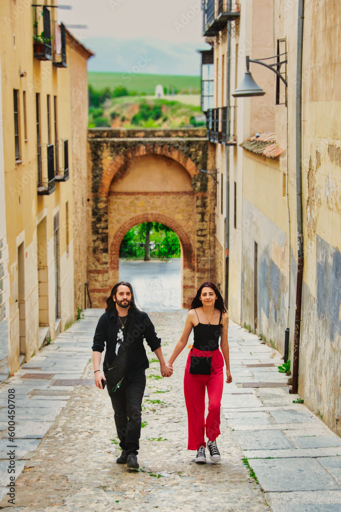 A young couple walk hand in hand through one of the streets of the old town of Segovia (Spain).