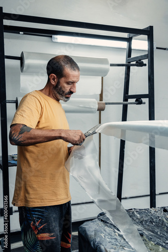 Focused man cutting fiberglass cloth on surfboard photo