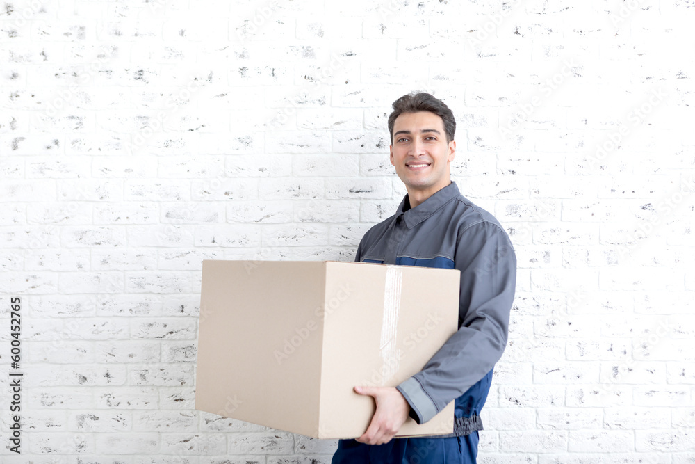 Handsome man from moving service carrying heavy box in front of white brick wall background Handsome man from moving service carrying heavy box in front of white brick wall background
