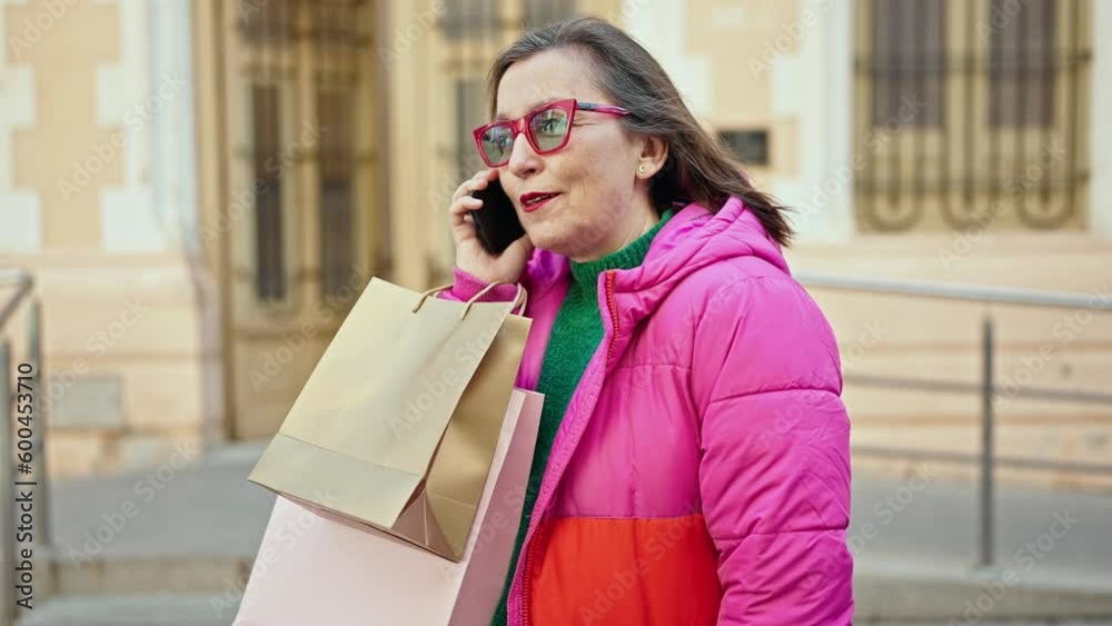 Mature hispanic woman with grey hair smiling going shopping speaking on the phone at street