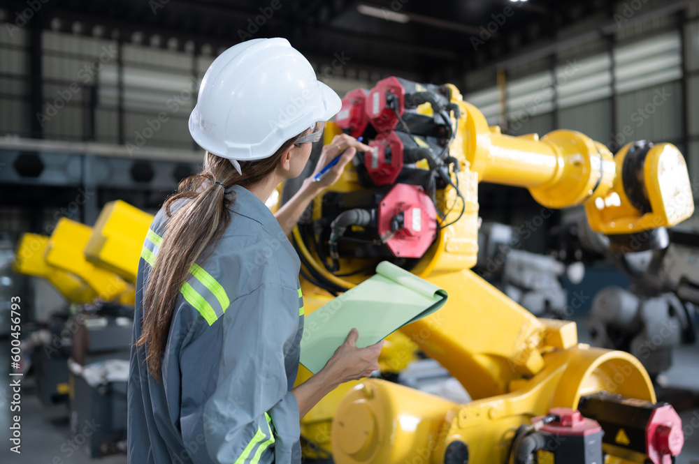 Fototapeta premium A female engineer checking documented items after installing a program on a robotic arm in a robotic warehouse and test the operation