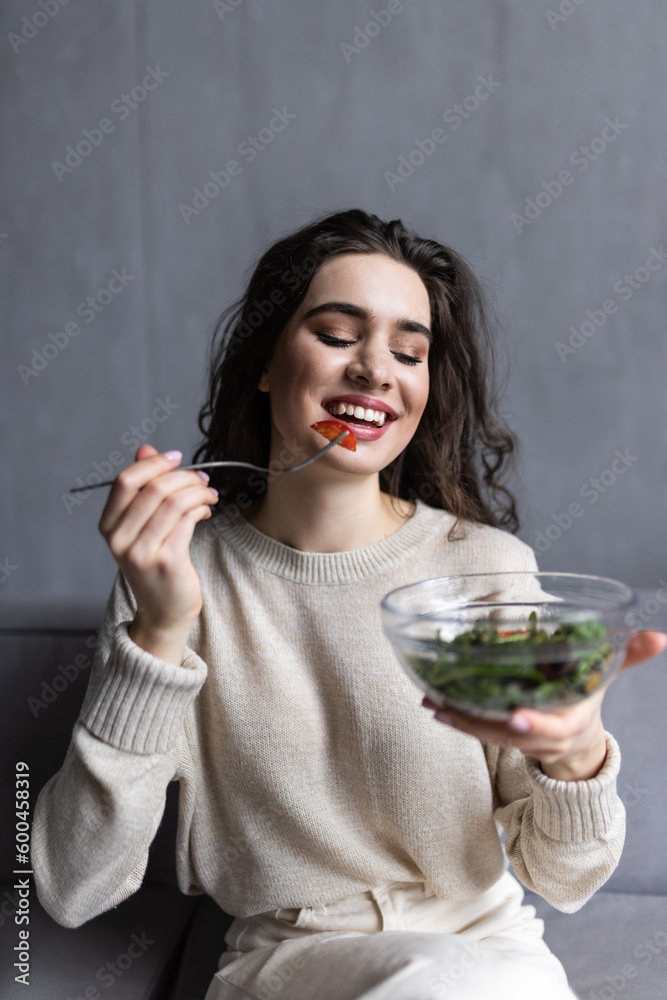 Happy youngwoman relaxing on the sofa eating salad in her living room Happy youngwoman relaxing on the sofa eating salad in her living room