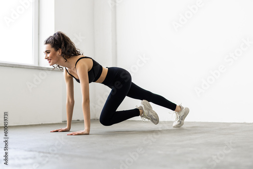 Young woman exercising at home, stretching legs in living room