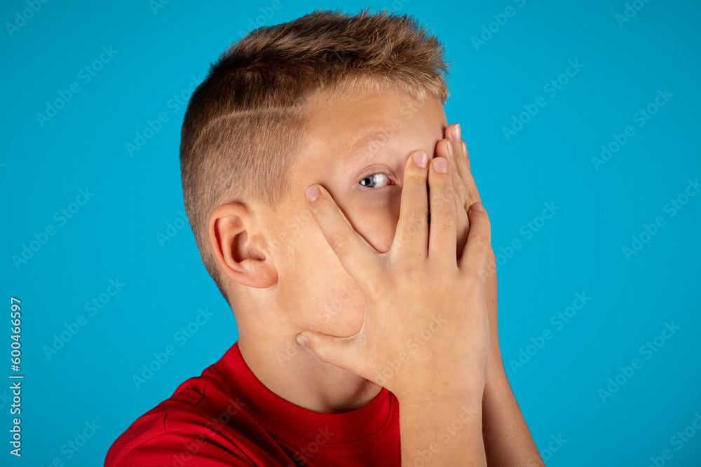 Shy preteen boy hiding face and peeking out through fingers Shy preteen boy hiding face and peeking out through fingers