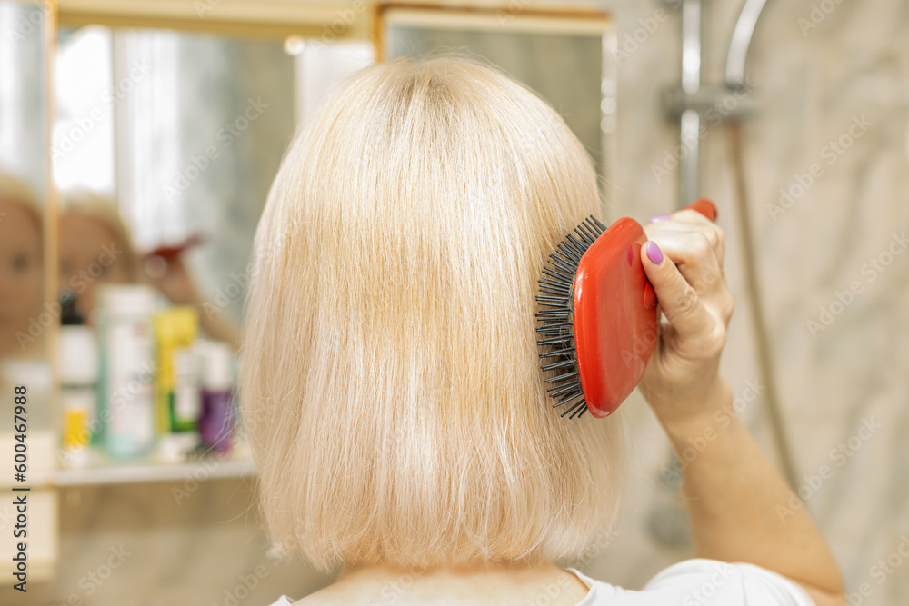 Fototapeta premium woman styling her hair while standing in front of a mirror.