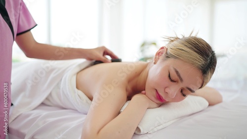 Close up face of beautiful Asian woman lying on massage bed while the masseuse is putting hot stones on back. Wellness and body relaxation therapy 